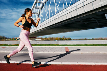 Young fitness woman running on a path next to a river and a bridge