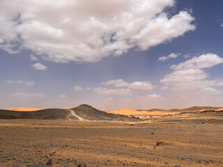 Fototapeta na wymiar Merzouga, Morocco, Africa, panoramic road in the Sahara desert in the Black Mountain area, with view of the black stones, fossils and sand dunes, 4x4 trip, blue sky and white clouds