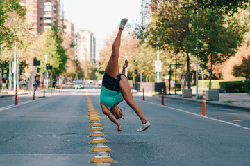 mujer morena con ropa urbana practicando capoeira en la ciudad y haciendo flexiones en medio de la calle. - obrazy, fototapety, plakaty