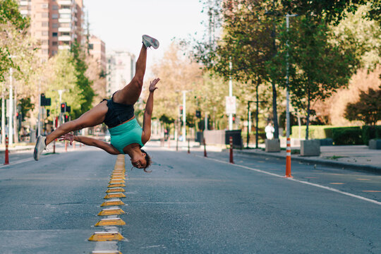 mujer morena con ropa urbana practicando capoeira en la ciudad y haciendo la rueda en medio de la calle.