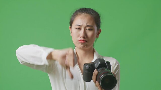 Close Up Of Upset Asian Photographer Looking At The Pictures In The Camera Then Showing Thumbs Down Gesture While Standing On Green Screen Background In The Studio
