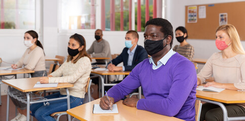 Fototapeta na wymiar African-american student wearing protective mask among students in university classroom