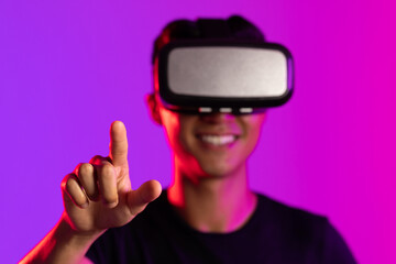 Portrait of happy asian man using vr headset pointing finger in studio with purple light