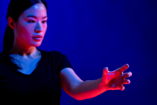 Asian woman making gesture with hand in studio with blue light with copy space