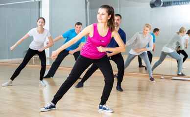 Fototapeta na wymiar Positive young woman trainer doing aerobics exercises with group of adult people in dance center