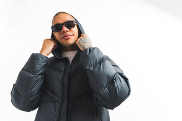 Street-style concept. Male crew member in sunglasses and black puffer jacket looking assertively to the camera and taking off his hood. White background. High quality photo © PoppyPix