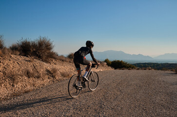 Fototapeta na wymiar Fit male cyclist riding dirt trails on gravel bike. Man riding gravel bike on gravel road in scenic view with hills in Spain. Sport motivation.Gravel road in mountains.