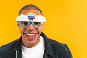 closeup shot of a young and cheerful Afro-American man wearing rainbow-shaped sunglasses on yellow background. High quality photo