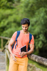 south asian 40s male hiking with a backpack in Asturias green countryside with a diary in spain.