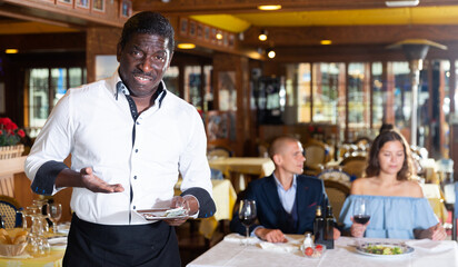 Fototapeta na wymiar Afro american waiter expressing displeasure with small tip in restaurant