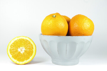 closeup of a bowl with oranges and an orange half on the table next to the bowl, white background