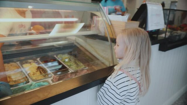 Cute little girl stands in front of an ice cream shop window. 