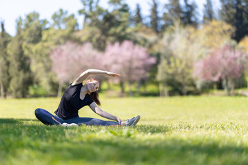 Yoga on nature - an adult woman sitting in lotus position and bending to the side with her leg...