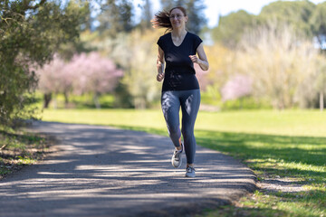 An adult smiling woman in tight grey leggings jogging on nature