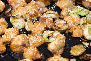 Cubes of teriyaki salmon covered in sesame seeds on oven pan coming out of air fryer