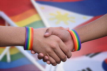 Closeup view of handshaking of LGBT people with blurred rainbow background, concept for success, cooperation, reconciliation, trust, and love for LGBT people and celebrations in pride month.