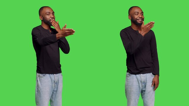 Young person in jeans giving air kisses to people in studio, posing with kissy face on green screen backdrop. Casual male model doing romantic gesture and feeling flirty, confident man.