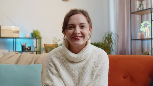 POV of young woman looking at camera, making video webcam conference call with friends family, enjoying pleasant conversation at home apartment. Portrait of girl laughing, waving hello on sofa in room