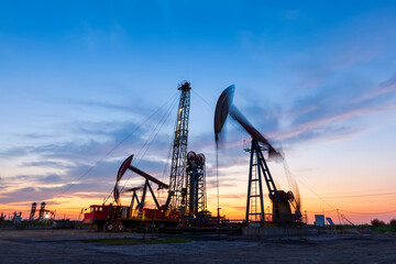 in the evening, oil pumps are running, The oil pump and the beautiful sunset reflected in the water, the silhouette of the beam pumping unit in the evening.