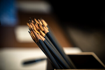 Arranged in a tidy row within a box at the desk, several gleaming black wooden pencils wait...