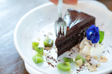 Chocolate cake on the white dish ready to eat, serve with kiwi slice and nut, decorated by butterfly pea.