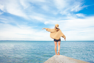 girl stands on a pier against the background of the sea and looks at the horizon, a woman in hat shows her hand into the sky, freedom concept