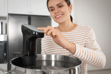 Woman using thermal immersion circulator in kitchen, focus on hand. Sous vide cooking