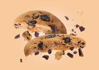 Tasty chocolate chip cookies falling on pale light brown background