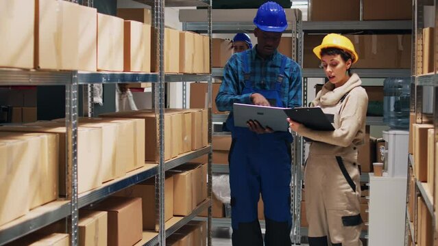Multiethnic team of employees working with goods and checking stock inventory on laptop, cargo in storage room. Depot workers analyzing industrial goods to plan distribution and shipment.