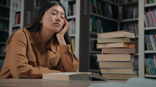 Tired sleepy asian woman student fall asleep in university library exhausted drowsy girl sleeping on desk with stack books feel fatigue doze sleep on table break from studying exam preparation concept