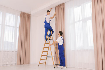 Fototapeta premium Workers in uniform hanging window curtain indoors