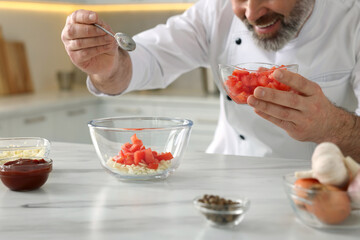 Professional chef making delicious tomato sauce at white marble table indoors, closeup