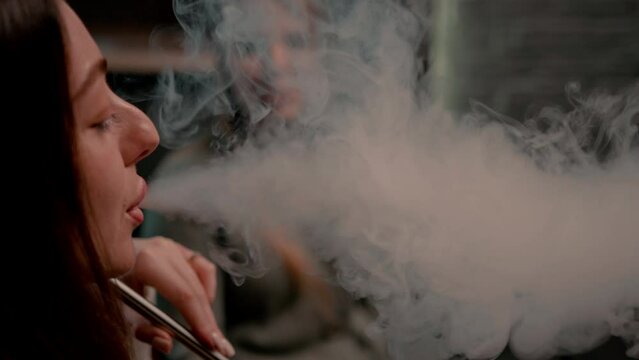 Beautiful young woman inhaling hookah girl smoking hookah sitting in lounge bar concept of relaxation and smoking