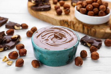 Bowl with tasty paste, chocolate pieces and nuts on white wooden table
