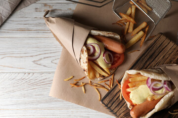Delicious pita wrap with sausages, vegetables and potato fries on white wooden table, top view....