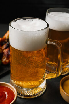 Mugs with delicious beer on dark grey table, closeup