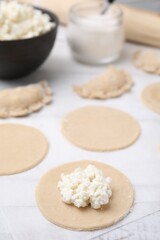 Fototapeta na wymiar Process of making dumplings (varenyky) with cottage cheese. Raw dough and ingredients on white table, closeup