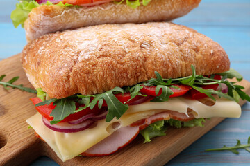 Delicious sandwich with fresh vegetables, cheese and arugula on wooden board, closeup