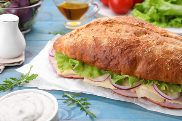 Delicious sandwich with fresh vegetables, cheese and arugula on light blue wooden table, closeup