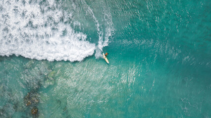 Surfer in the blue transparent ocean in Hawaii from above, aerial drone shot.