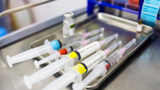 A medical syringe with a colorful tag label on stainless tray in hospital.Drug preparation for patient sedation before surgery with blur background.Close up macro photo of syringes with medicine.