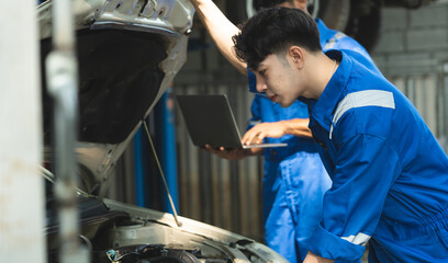 A team of Asian mechanics use their laptop computers to view engine maintenance history for inspections and perform engine room checks at car and maintenance workshops.
