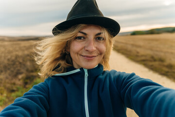 girl in a hat on the background of the field makes a selfie