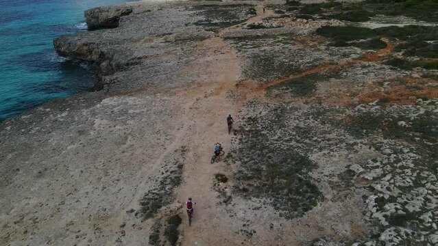 Aerial drone footage following riders along clifftops in Menorca. Dusty trail lie ahead for cyclists.