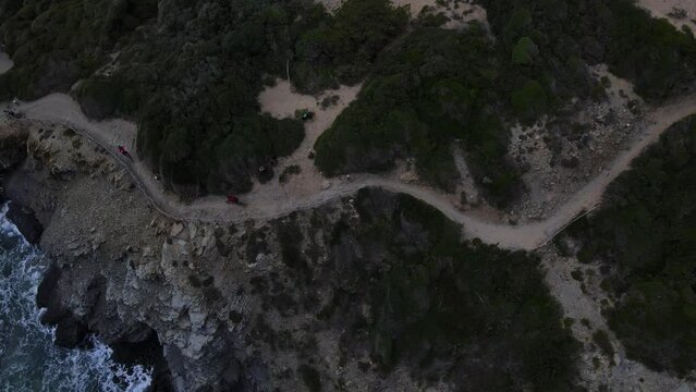 Birds Eye view of cyclists riding along coastal track with waves washing against the cliffs.