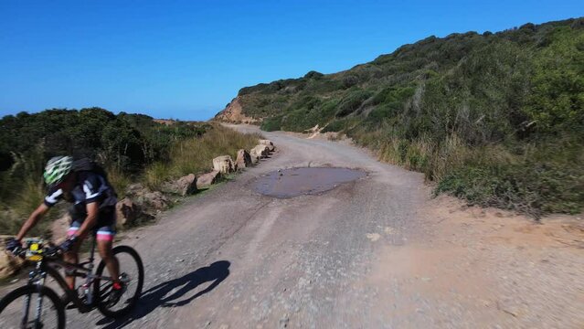 Mountain bike rider going through puddle on gravel part of race track.