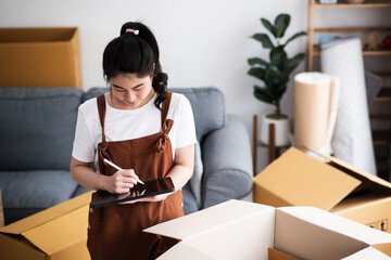 New house, asian woman check list of stuff in the box while feeling proud and excited about buying...