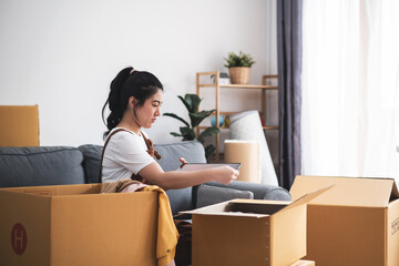 Fototapeta na wymiar New house, asian woman check list of stuff in the box while feeling proud and excited about buying a house with a mortgage loan. Young asian woman first time buyers unpacking in dream home.
