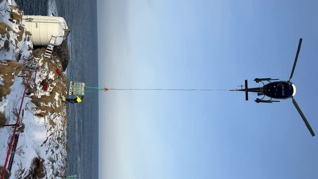 Worker directing container from helicopter with longline to a certain position outside in the Arctic Circle, Vertical shot