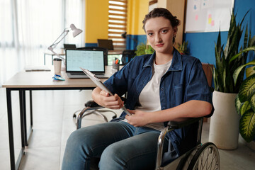 Young businesswoman with disability sitting in wheelchair with clipboard